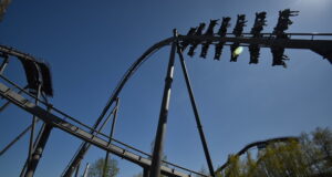 We Love The Swarm at Thorpe Park — And Here’s Why A steel roller coaster loop under a clear blue sky, with riders on a cars train zooming along the track.