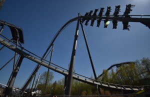 We Love The Swarm at Thorpe Park — And Here’s Why A steel roller coaster loop under a clear blue sky, with riders on a cars train zooming along the track.