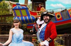 Princesses, Pirates & Pure Family Chaos: Gulliver’s Bank Holiday Takeover Princess in a light blue gown posing with a man in a red pirate coat beside a colorful ship at a theme park.