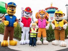 Chessington PAW Patrol Land Tickets: Prices, Dates & How to Save Money Young child in a yellow safety vest and helmet holding a clipboard, posing with five large costumed rescue-dog characters at a park attraction.