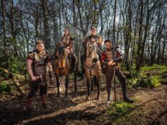 Viking Raiders Storms Warwick Castle in 2026: A Bold New Era of Live Entertainment Four armored riders on horseback in a sunlit forest, wearing fur cloaks and leather armor, ready for battle.