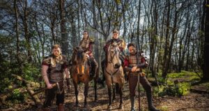 Viking Raiders Storms Warwick Castle in 2026: A Bold New Era of Live Entertainment Four armored riders on horseback in a sunlit forest, wearing fur cloaks and leather armor, ready for battle.