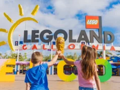 LEGOLAND Resorts Unveils Exciting FIFA® World Cup 2026 Celebration Two kids in blue and pink shirts raise a golden LEGO trophy in front of the Legoland California entrance sign under a blue sky. misión