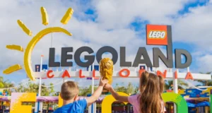 LEGOLAND Resorts Unveils Exciting FIFA® World Cup 2026 Celebration Two kids in blue and pink shirts raise a golden LEGO trophy in front of the Legoland California entrance sign under a blue sky. misión