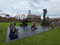 We Attended Valgard’s Opening Day — Here’s Why It Works So Well Fire performers on an outdoor stage display flames while wearing Viking-inspired costumes, with a red roller-coaster track and cheering audience nearby.