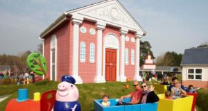 Grandpa Pig’s Little Train to Close Briefly for Essential Maintenance Colorful children's train ride with a Peppa Pig figure, red engine and blue/yellow cars, carrying families past a pink building.