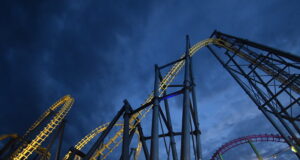 Late Night Rides Are Back This May Half-Term at Fantasy Island Nighttime view of illuminated roller coasters with yellow and blue tracks twisting against a dark blue sky