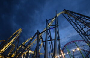 Late Night Rides Are Back This May Half-Term at Fantasy Island Nighttime view of illuminated roller coasters with yellow and blue tracks twisting against a dark blue sky