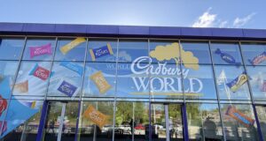 Sweet Savings at Cadbury World – Midweek Tickets from Just £18pp! Glass storefront with colorful Cadbury Roses decals across the windows and a large 'Cadbury World' sign on blue-framed panels.