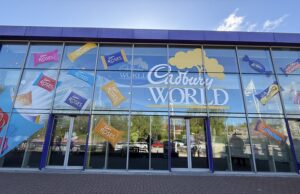 Sweet Savings at Cadbury World – Midweek Tickets from Just £18pp! Glass storefront with colorful Cadbury Roses decals across the windows and a large 'Cadbury World' sign on blue-framed panels.