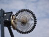 What’s Happening at UK Theme Parks This Week (Week of 18 May 2026) Close-up of a large roller coaster wheel with passenger cars around the rim, chrome spokes radiating from the center against a blue sky.