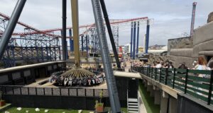 Pictures Showing AVIKTAS at Blackpool Pleasure Beach: The UK’s New Giant Swing Dominates the Skyline Amusement park ride with a circular rotating gondola around a tall central column; roller coasters visible in the background.