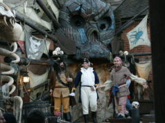 We Can’t Be the Only Ones Still Missing the Pirate Show in Mutiny Bay Three performers in pirate costumes center stage in a steampunk pirate set with a large mechanical creature face above and skulls nearby.