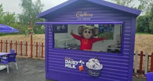 Gulliver’s Theme Parks Launch New Froneri Ice Cream Partnership Across UK Resorts Purple Cadbury Dairy Milk ice cream kiosk with mascot waving behind the window; outdoor seating nearby with purple chairs and umbrella.