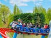 PAW Patrol Opens at Chessington World of Adventures: Everything You Need to Know About the UK’s First Pup-Themed Land Riders on a blue roller-coaster train outdoors, smiling, with a mascot in the front car and trees in the background.