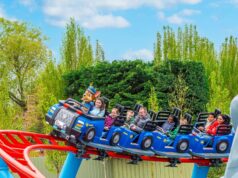 PAW Patrol Opens at Chessington World of Adventures: Everything You Need to Know About the UK’s First Pup-Themed Land Riders on a blue roller-coaster train outdoors, smiling, with a mascot in the front car and trees in the background.