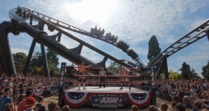 Drayton Manor’s Rock ’n’ Rumble: Wrestling, Country Music and Theme Park Thrills Two wrestlers face off inside an outdoor ring as a referee watches, with a large cheering crowd and a roller coaster in the background.