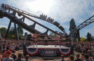 Drayton Manor’s Rock ’n’ Rumble: Wrestling, Country Music and Theme Park Thrills Two wrestlers face off inside an outdoor ring as a referee watches, with a large cheering crowd and a roller coaster in the background.