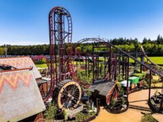 Drakon at Paultons Park: Ride Guide, Height Restrictions & Accessibility Red steel roller coaster with tall looping track in a sunny outdoor amusement park, with trees and blue sky in the background.