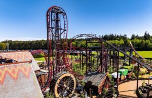 Drakon at Paultons Park: Ride Guide, Height Restrictions & Accessibility Red steel roller coaster with tall looping track in a sunny outdoor amusement park, with trees and blue sky in the background.