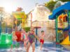 Drench Towers & Splash Safari Reopening at LEGOLAND Windsor This May Children laugh and run through a colorful water park with sprinklers and fountains on a sunny day—water splashes around them.