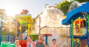 Drench Towers & Splash Safari Reopening at LEGOLAND Windsor This May Children laugh and run through a colorful water park with sprinklers and fountains on a sunny day—water splashes around them.