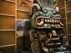 Step Inside the Forbidden Chamber: Movie Park Germany’s New Attraction Large carved totem head with bold facial features inside a studio with metal truss structures surrounding it