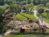 What’s Happening at UK Theme Parks This Week (Week of 25 May 2026) Elevated view of a bright yellow roller coaster with purple rails and a 'Barnyard Whirl' sign, set among green trees and park paths.