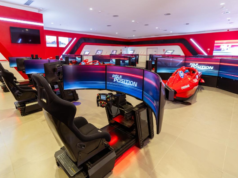 Experience the Ferrari GP Festival at PortAventura World’s Ferrari Land Indoor racing simulators: curved-screen cockpits arranged around a red Formula-style race car in a bright red-lit room.