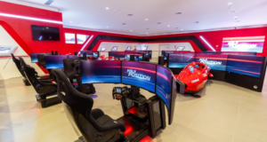 Experience the Ferrari GP Festival at PortAventura World’s Ferrari Land Indoor racing simulators: curved-screen cockpits arranged around a red Formula-style race car in a bright red-lit room.
