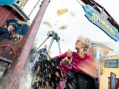 Stormvåg Makes Its Debut – Liseberg Opens a Brand-New Family Ride Older woman with gray hair and pink feather boa, holding an ice cream cone as water splashes from a carnival ride nearby