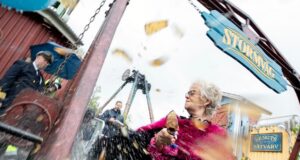 Stormvåg Makes Its Debut – Liseberg Opens a Brand-New Family Ride Older woman with gray hair and pink feather boa, holding an ice cream cone as water splashes from a carnival ride nearby