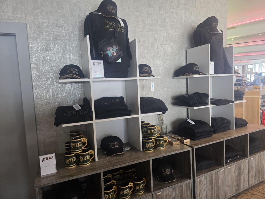 Store display featuring AVIKTAS branded hoodies, hats, and mugs on grey shelves.