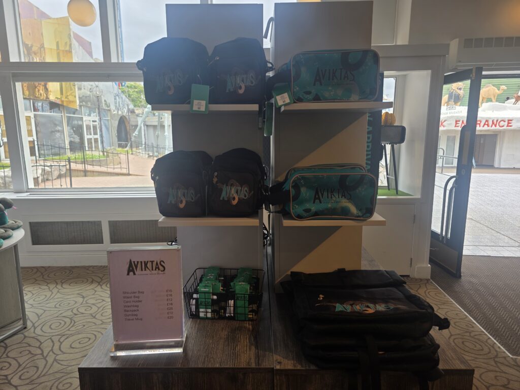 Display of Aviktas brand backpacks and bags on shelves by a window, with teal and black bags visible and a price list in front.