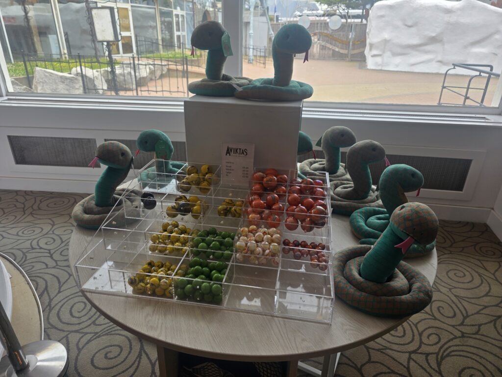 Colorful glass marbles in a clear display case surrounded by teal plush snakes inside a shop window.