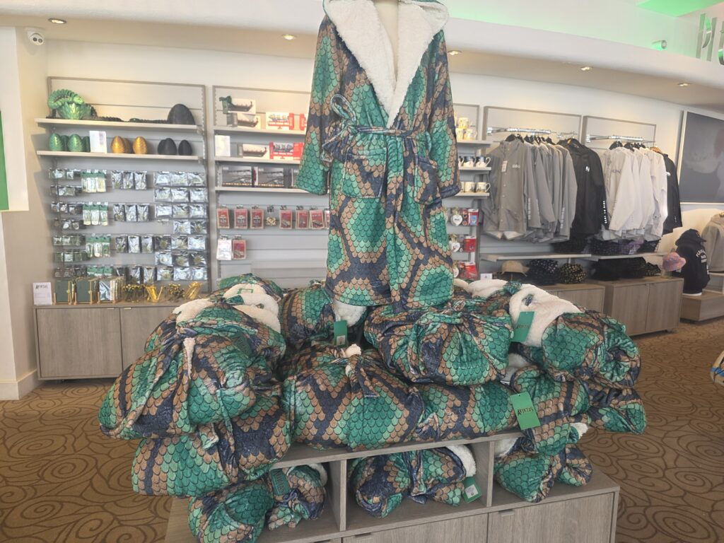 Tall display of green and brown snake-print robes wrapped around a mannequin in a clothing store, with shelves of accessories in the background.