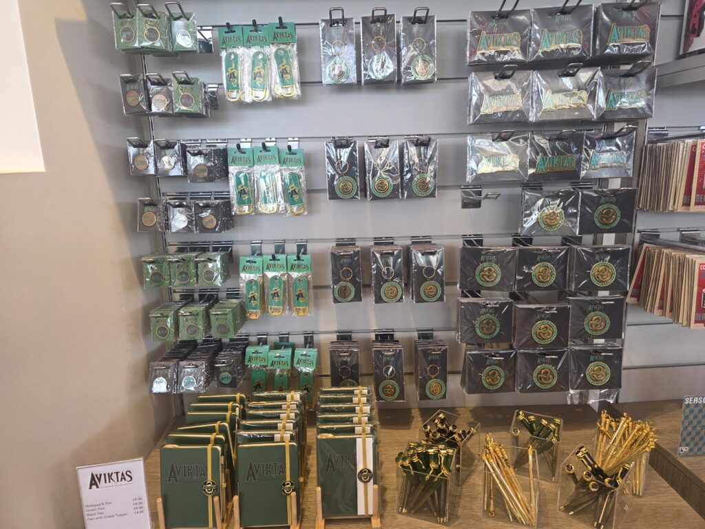 Display of Aviktas-branded items: green notebooks, pens, and keychains in plastic packaging on a wall rack