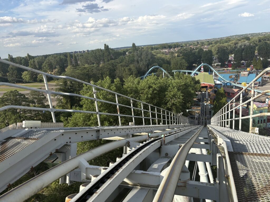 View from a roller coaster track above green trees, with a distant town and blue sky with clouds