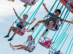 Great British Summer Savings at Harbour Park Children joyfully ride on a colorful carnival swing ride high in the air against a bright blue sky.