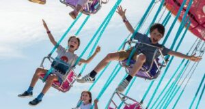 Great British Summer Savings at Harbour Park Children joyfully ride on a colorful carnival swing ride high in the air against a bright blue sky.