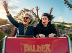 Liseberg and Professor Micael Dahlen launch research initiative on happiness Woman in blue blazer and green scarf waves joyfully on a roller coaster ride beside a terrified young man in a black hoodie; amusement park background with roller coaster and Ferris wheel under a blue sky (motion blurred).