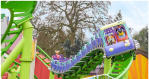 Visit the NEW World of PAW Patrol at Chessington, Then Ride NEW Bluey the Ride at Alton Towers – For FREE! Riders scream with excitement on a blue roller coaster car traveling along bright green tracks outdoors at a theme park
