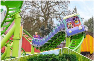 Visit the NEW World of PAW Patrol at Chessington, Then Ride NEW Bluey the Ride at Alton Towers – For FREE! Riders scream with excitement on a blue roller coaster car traveling along bright green tracks outdoors at a theme park