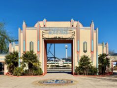 Celebrate 30 Years: Movie Park Germany’s Summer Lineup Entrance to Movie Park Germany with pastel Art Deco arches and turquoise accents, flanked by palm trees against a blue sky.",