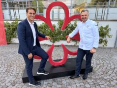 Multisensory fine dining restaurant Eatrenalin awarded first Michelin star Two men in smart outfits pose next to a large red abstract sculpture outdoors, standing on a black pedestal.