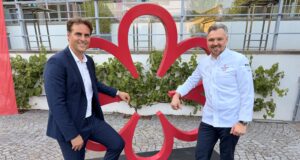 Multisensory fine dining restaurant Eatrenalin awarded first Michelin star Two men in smart outfits pose next to a large red abstract sculpture outdoors, standing on a black pedestal.