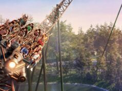 Nigloland Announces SUPERSONIC 1887 Roller Coaster for 2027 Roller coaster train filled with riders plunges around a curve over a forested amusement park backdrop, sunset light.