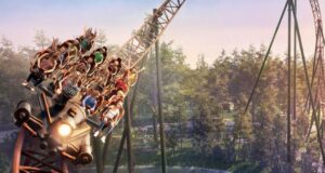 Nigloland Announces SUPERSONIC 1887 Roller Coaster for 2027 Roller coaster train filled with riders plunges around a curve over a forested amusement park backdrop, sunset light.