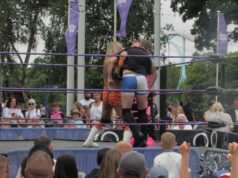 What’s Happening at UK Theme Parks This Week (Week of 6 July 2026) Two wrestlers hug in a ring with purple ropes while a crowd watches in a park setting.