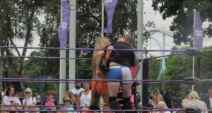 What’s Happening at UK Theme Parks This Week (Week of 6 July 2026) Two wrestlers hug in a ring with purple ropes while a crowd watches in a park setting.